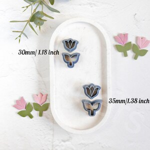 May include: Two sets of flower cookie cutters, one set is 1.18 inches and the other is 1.38 inches. The larger set is on a white oval plate. Both sets are blue and feature a tulip design.