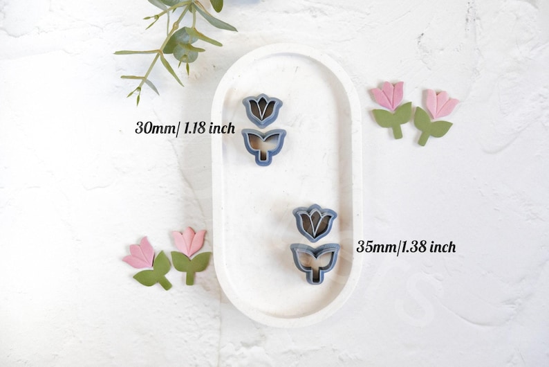May include: Two sets of flower cookie cutters, one set is 1.18 inches and the other is 1.38 inches. The larger set is on a white oval plate. Both sets are blue and feature a tulip design.