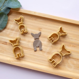 May include: Five cookie cutters shaped like dogs on a wooden surface. The cookie cutters are made of a light brown plastic material.