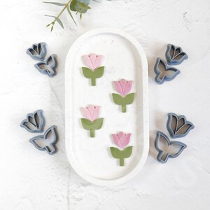 May include: A set of six cookie cutters in the shape of tulips. The cutters are made of blue plastic and have a smooth finish. There are three pink and green tulip cutters and three blue tulip cutters.