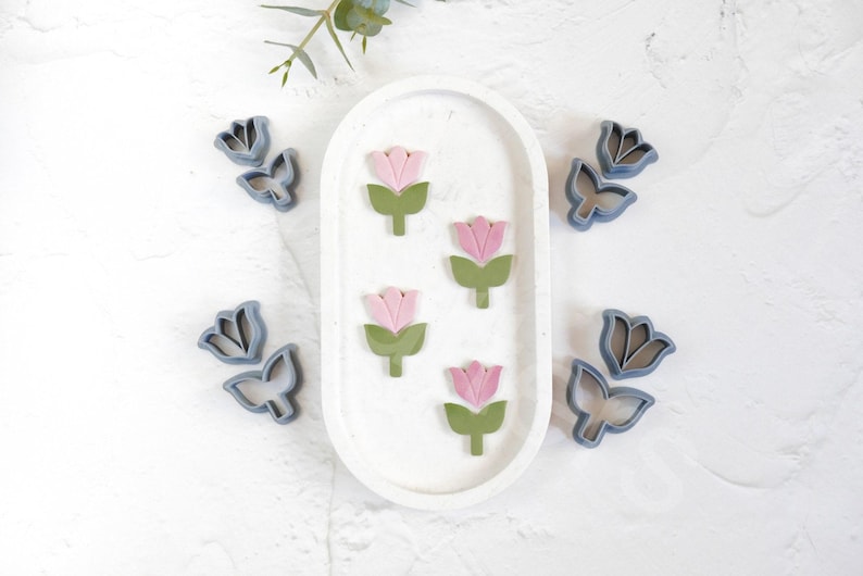 May include: A set of six cookie cutters in the shape of tulips. The cutters are made of blue plastic and have a smooth finish. There are three pink and green tulip cutters and three blue tulip cutters.