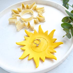 Puede incluir: Un plato amarillo en forma de sol con un anillo en su interior. El plato está sobre un plato blanco con un cortador de galletas en forma de sol.