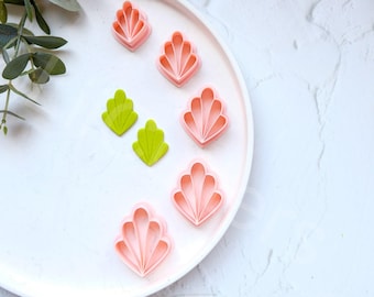 May include: A white plate with five pink and two green plastic cookie cutters shaped like seashells and leaves.