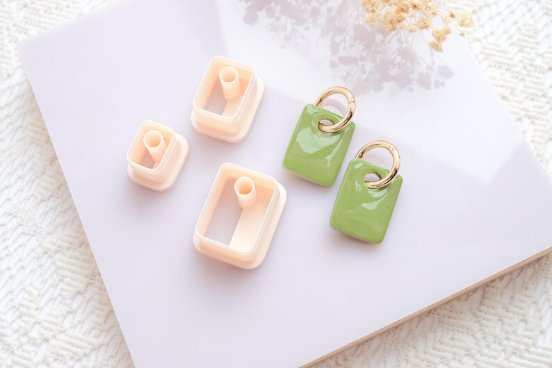 Puede incluir: Un conjunto de suministros para manualidades, que incluye tres cortadores de arcilla polim&eacute;rica de color melocot&oacute;n claro en forma rectangular y dos pendientes verdes con aros dorados. Los pendientes tienen un acabado brillante.