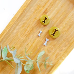 May include: Three dog bone shaped cookie cutters on a wooden surface. Two of the cutters are green and one is light blue.