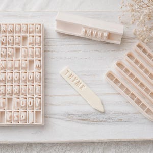 May include: A set of off-white plastic tools for clay or dough, including a rectangular grid tray filled with individual letter stamps, a long rectangular stamp holder with the word THYME, four pointed plant markers, and one marker labeled THYME.