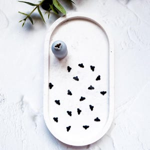 Puede incluir: Una bandeja ovalada blanca con un jarrón gris y confeti negro en forma de corazón.