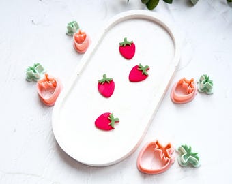 Może przedstawiać: Zestaw plastikowych foremek do ciasteczek w kolorze różowym i zielonym w kształcie truskawek i marchewek. Formy ułożone są na białym tle.