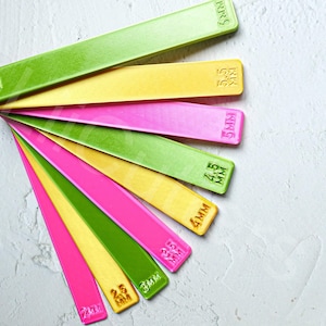 May include: A set of seven colourful plastic rulers with different measurements in millimetres. The rulers are arranged in a fan shape, with the largest ruler at the top and the smallest ruler at the bottom. The rulers are green, yellow, pink, and green.