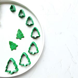 Könnte beinhalten: Ein weißer Teller mit neun grünen Plätzchenausstechern in Form von Weihnachtsbäumen, die in einem Kreis angeordnet sind.