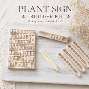 May include: A plant sign builder kit featuring a rectangular tray filled with individual letter stamps, a wooden holder containing the word THYME, four blank pointed plant stakes, and one stake embossed with the word THYME in white plastic.
