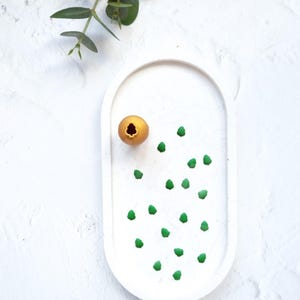 Può includere: Un piatto ovale bianco con un oggetto dorato a forma di uovo e decorazioni a forma di albero verde.