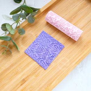 May include: Two rolling pins for baking, one purple and one pink, with a leaf pattern. The rolling pins are on a wooden surface.