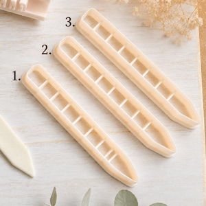 May include: Three off-white plastic cookie cutters labeled 1, 2, and 3, each featuring a long, narrow, rectangular shape with rounded ends and internal cross-bar dividers. The cutters are arranged diagonally on a light-colored surface.