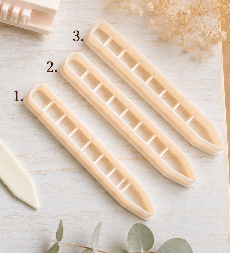 May include: Three off-white plastic cookie cutters labeled 1, 2, and 3, each featuring a long, narrow, rectangular shape with rounded ends and internal cross-bar dividers. The cutters are arranged diagonally on a light-colored surface.