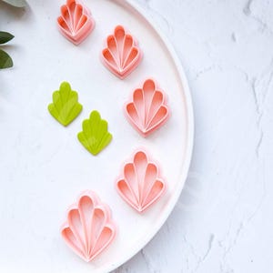 May include: A white plate with five pink and two green plastic cookie cutters shaped like flowers and leaves. The plate is on a white marble surface.