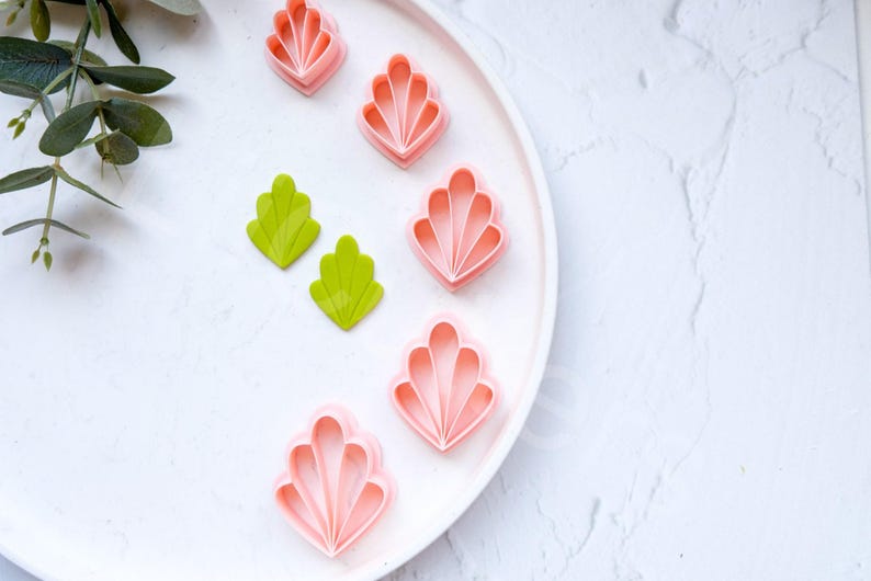 May include: A white plate with five pink and two green plastic cookie cutters shaped like flowers and leaves. The plate is on a white marble surface.