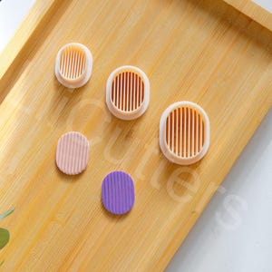 May include: Four round cookie cutters on a wooden surface. The cutters are in different sizes and colors, including pink, purple, and white.