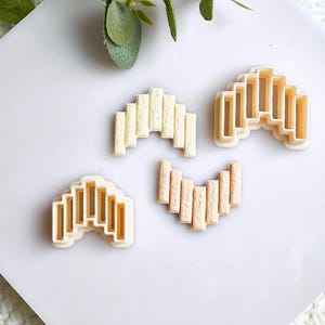 May include: Four cookie cutters in various shapes. The cutters are in the shape of a series of vertical rectangles, arranged in an arch. The cutters are in shades of beige and tan.