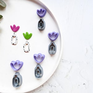 May include: A white plate with a variety of cookie cutters. The cutters are shaped like flowers and have a variety of colors, including purple, green, and pink.