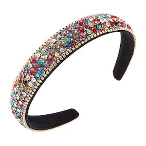 May include: A colorful headband with a black base, adorned with a multitude of sparkling rhinestones in various colors. The rhinestones are set in a gold-toned metal band, creating a glamorous accessory. The headband is approximately 1 inch wide.