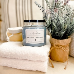 May include: A blue glass candle jar with a black lid and a white label that reads "Canyon Scents Lavender Chamomile The Gold Standard in Premium Fragrance". The candle is sitting on a white towel and a burlap bag filled with lavender.