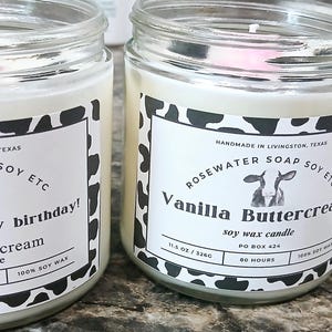 Może przedstawiać: Trzy szklane słoiki z białymi pokrywkami i czarno-białymi etykietami z nadrukiem krowy. Etykiety głosiły "Rosewater Soap Soy Etc" i przedstawiają ilustrację krowy. Słoiki zawierają świece sojowe o zapachach "Moove over, it's my birthday! Vanilla Buttercream", "Vanilla Buttercream" i "Hay Happy Vanilla Buttercream".