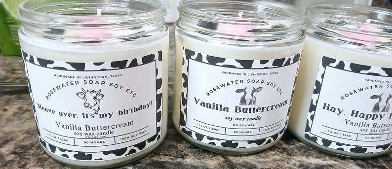 Może przedstawiać: Trzy szklane słoiki z białymi pokrywkami i czarno-białymi etykietami z nadrukiem krowy. Etykiety głosiły "Rosewater Soap Soy Etc" i przedstawiają ilustrację krowy. Słoiki zawierają świece sojowe o zapachach "Moove over, it's my birthday! Vanilla Buttercream", "Vanilla Buttercream" i "Hay Happy Vanilla Buttercream".