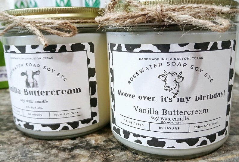 Może przedstawiać: Dwa szklane słoiki z białymi pokrywkami i czarno-białymi etykietami z nadrukiem krowy. Etykiety głosi: "Handmade in Livingston, Texas, Rosewater Soap Soy Etc, Moove over, it's my birthday! Vanilla Buttercream Soy Wax Candle, 11.5 oz / 326g, PO Box 424, 80 Hours, 100% Soy Wax".
