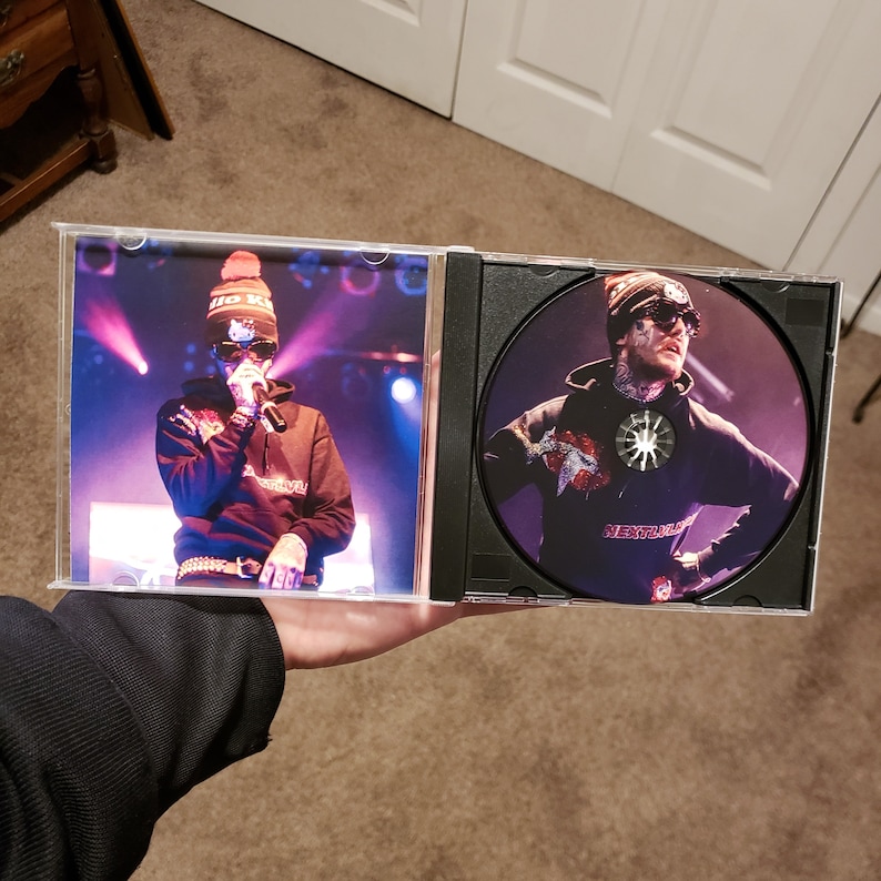 Puede incluir: Una caja de CD con una foto en blanco y negro de una persona que lleva una sudadera con capucha negra, un gorro rojo y gafas de sol. La caja de CD est&aacute; abierta y el CD es visible. El CD tiene una foto de la misma persona que lleva una sudadera con capucha negra y un gorro negro. El texto "Neutral" es visible en el CD.