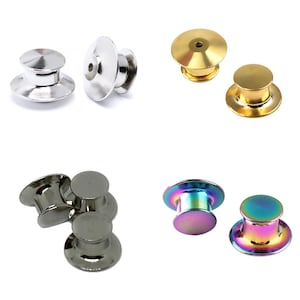 May include: Assortment of metal pin backs in various colors and finishes, including silver, gold, and iridescent. The pin backs are designed for attaching pins, badges, and other accessories to clothing or fabric.