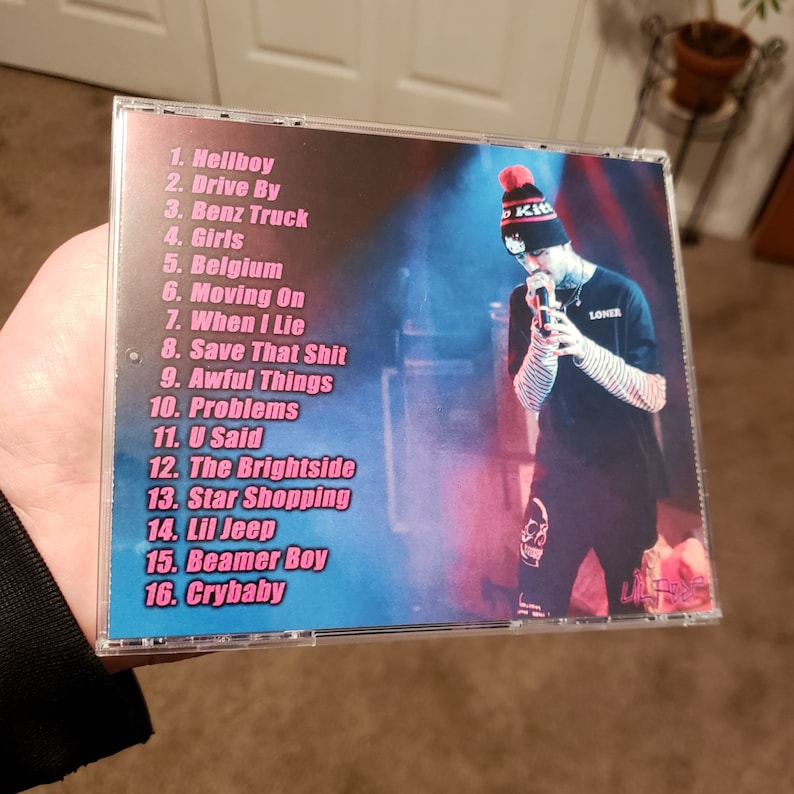 Puede incluir: Una caja de CD con un dise&ntilde;o rosa y azul que presenta a una persona con una camisa a rayas blancas y negras y un gorro rojo y blanco. El texto en la caja enumera los t&iacute;tulos de las canciones: Hellboy, Drive By, Benz Truck, Girls, Belgium, Moving On, When I Lie, Save That Shit, Awful Things, Problems, U Said, The Brightside, Star Shopping, Lil Jeep, Beamer Boy, Crybaby.
