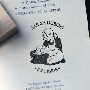 Può includere: Illustrazione in bianco e nero di una donna che lavora a un tornio, con il testo "SARAH DUBOIS" e "EX LIBRIS". Un timbro di legno è visibile nell'angolo in alto a sinistra. L'immagine è tratta da un libro.