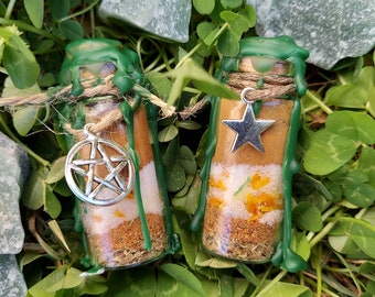 May include: Two small glass bottles with green wax seals and charms. The bottles contain layers of brown, white, and orange materials. One charm is a silver pentagram, the other is a silver star.