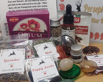 May include: A collection of small jars and pouches containing various herbs and seeds, including lavender, poppy seeds, mint, and pomegranate seeds. There is also a bottle of ritual oil, a small jar of garnet, and a few stones. The jars and pouches are labeled with the names of the herbs and seeds. The image also includes a small box with the word "OPIUM" printed on it.