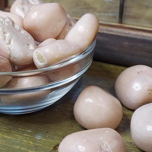 May include: A bowl filled with smooth, pale pink tumbled stones. The stones are arranged in a random pattern and have a glossy finish.