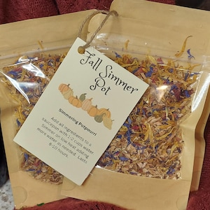 May include: Two clear plastic bags filled with dried potpourri, with a kraft paper tag attached. The tag reads "Fall Simmer Pot" and features a pumpkin illustration. The potpourri includes dried flowers and herbs.
