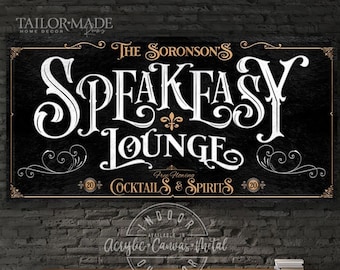 May include: Black rectangular sign with gold trim and white lettering that reads "The Soronson's Speakeasy Lounge". The sign also says "Free Flowing Cocktails & Spirits". The sign is displayed indoors.
