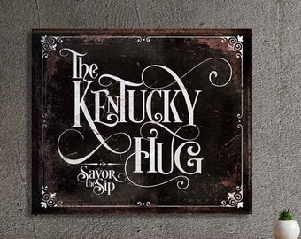 May include: A black and white sign with the text "The Kentucky Hug" and "Savor the Sip" in a vintage style font. The sign has a distressed, rustic look.