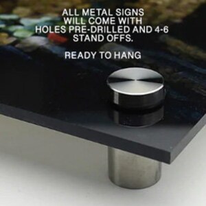 May include: A black metal sign with a silver stand-off. The sign has the text "ALL METAL SIGNS WILL COME WITH HOLES PRE-DRILLED AND 4-6 STAND OFFS. READY TO HANG."