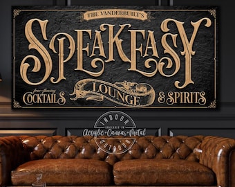 May include: A rectangular wall sign with a black textured background and gold lettering. The text reads THE VANDERBUILT'S SPEAKEASY LOUNGE & SPIRITS with free-flowing COCKTAILS. The design features decorative scrollwork and borders in a gold finish.