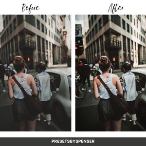 May include: A woman in a white vest top and black shorts walks down a city street. She is carrying a brown leather bag over her shoulder. The street is lined with buildings and there are other people walking around.