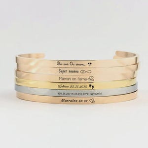 Könnte beinhalten: Stapel von sechs Metallarmreifen in Gold-, Silber- und Roségoldtönen. Jedes Armband ist mit einer anderen Botschaft und kleinen Symbolen graviert. Die Armbänder sind übereinander gestapelt.