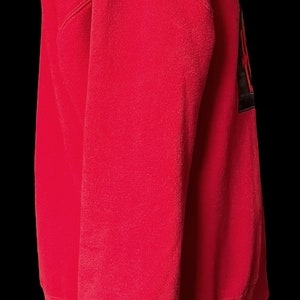 May include: A red sweatshirt with a black and white graphic on the front. The sweatshirt has a ribbed collar and cuffs.