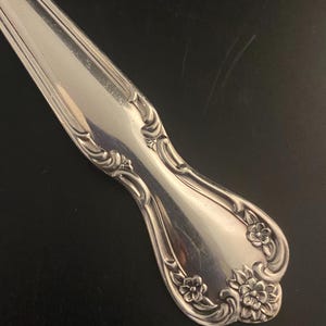 May include: Close-up of the ornate handle of a silver spoon with a floral design.