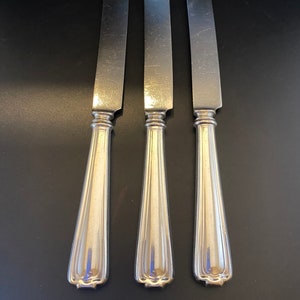 May include: Three silver butter knives with ornate handles.