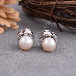 May include: A pair of pearl earrings with a silver setting. Each earring features a single pearl surrounded by small sparkling stones.