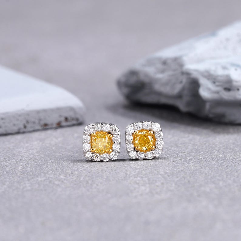 May include: A pair of square-shaped diamond earrings with a yellow center stone surrounded by a halo of smaller white diamonds.
