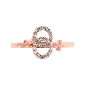May include: A rose gold ring with a double circle design set with small diamonds. The circles are connected by a small arrow and a cross.