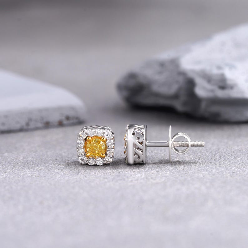 May include: A pair of gold earrings with a square-shaped yellow diamond in the center of each earring. The diamonds are surrounded by a halo of smaller diamonds.